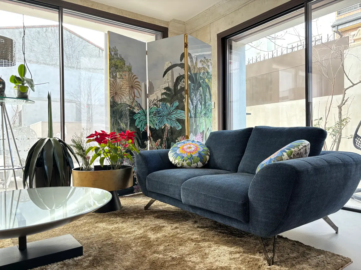 Salón con sofá azul y mural vegetal.