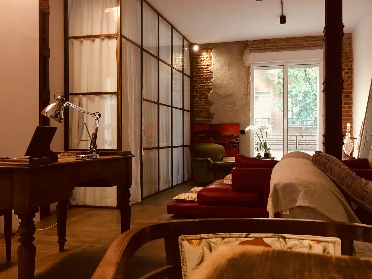 Estudio con mampara de vidrio y salón con sofá rojo.