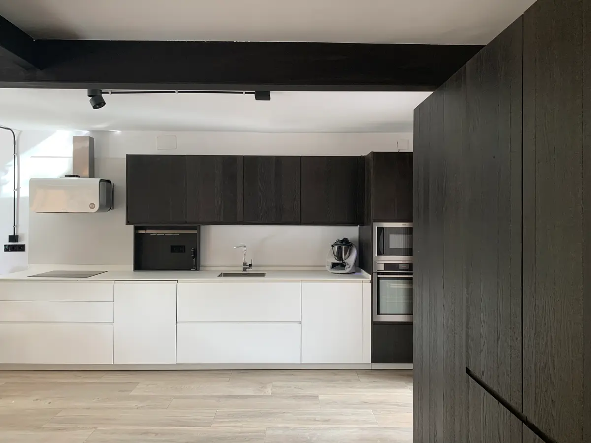 Cocina blanca con muebles altos en madera oscura.