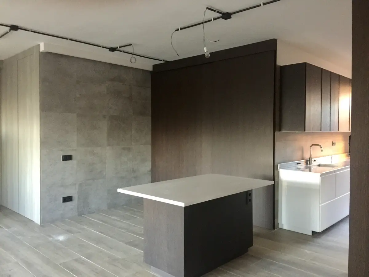 Cocina con isla de piedra clara y pared de hormigón.